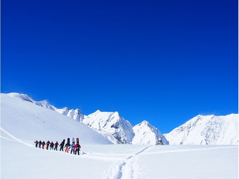 Backcountry A group climbing a snowy mountain with snowboards on their backs Sunny weather