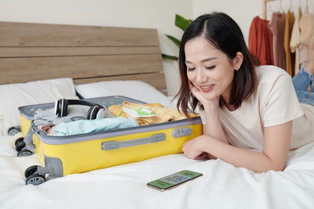 A woman collecting information on a smartphone while preparing for a trip on the bed