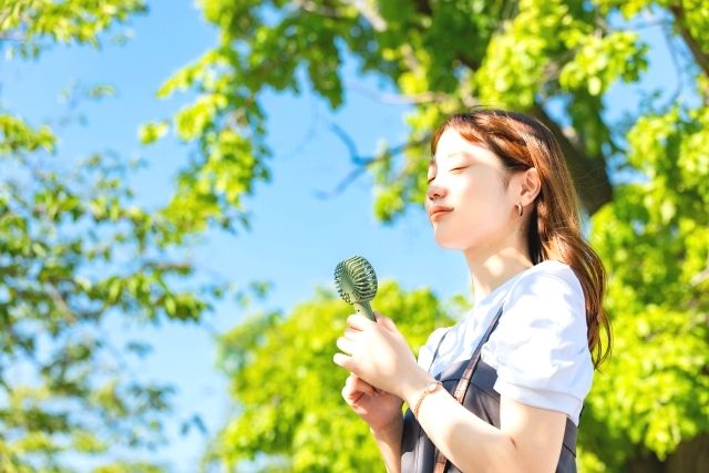 A woman cooling off with a small fan at a campsite