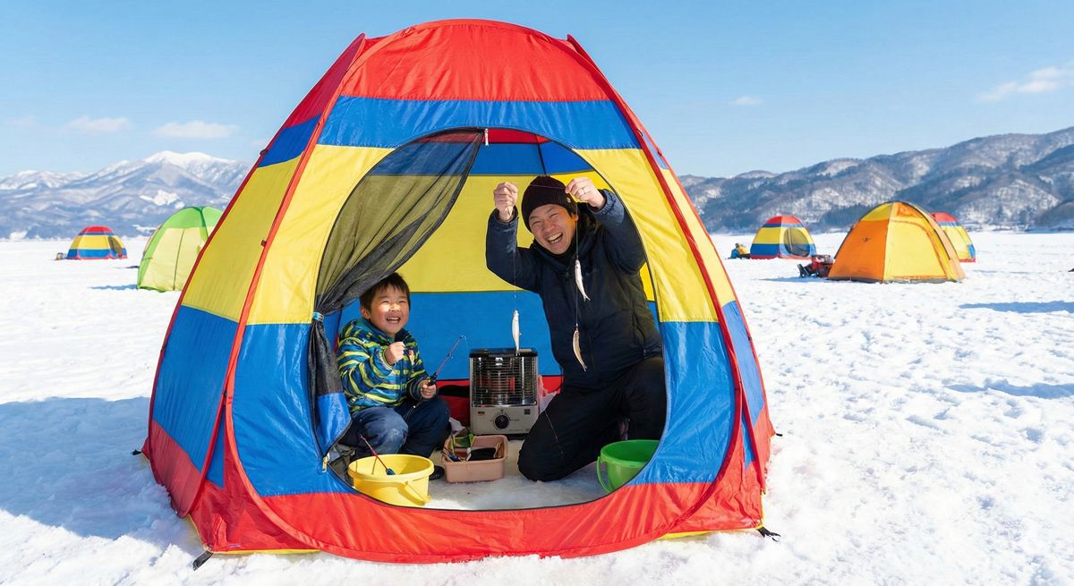 凍結した野尻湖の氷上で、カラフルなテントの中から笑顔でワカサギを釣り上げる親子