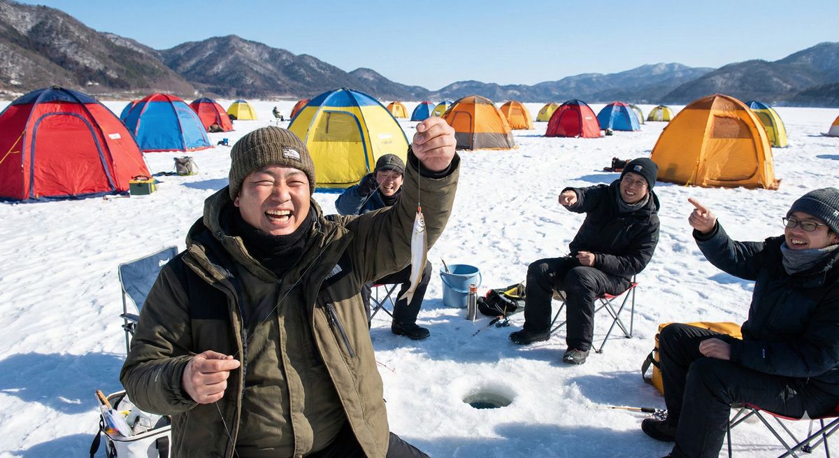 真っ白に凍った湖の上、カラフルなテントが並ぶ。氷の穴からワカサギを釣り上げ、とびきりの笑顔を見せる様子