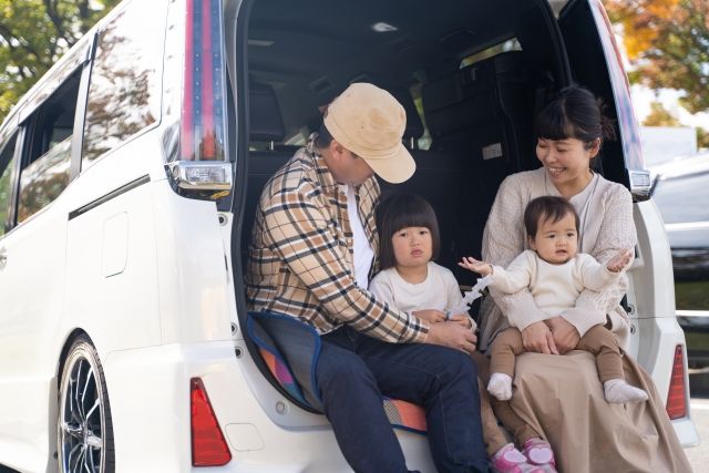 Parents and children sitting in the luggage space of a one-box car and relaxing